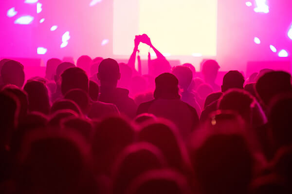 Huge concert going crowd bathed in neon pink light.